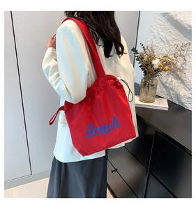 Detail of red drawstring tote bag with Beach print worn over a white suit jacket