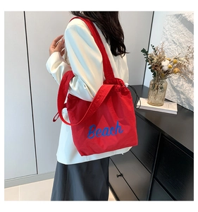 Detail of red drawstring canvas tote bag featuring blue Beach lettering and wide shoulder strap