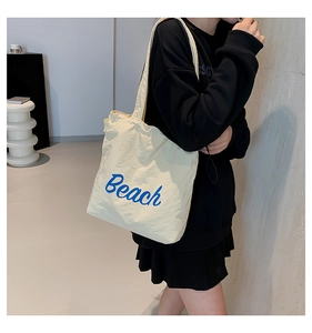 Detail of canvas shoulder bag with blue Beach lettering and long handles on a model