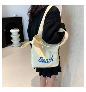 Detail view of cream canvas tote bag featuring blue Beach lettering and soft fabric texture