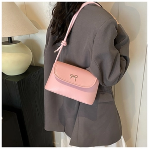 Model wearing a pink shoulder bag with a metal bow buckle and minimalist design