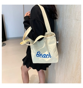 Detail of cream tote bag featuring blue Beach text and functional drawstring closure