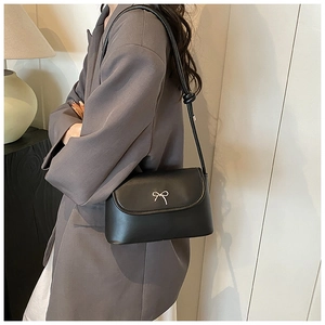 Detail of elegant black shoulder bag featuring a silver bow buckle and matte leather texture