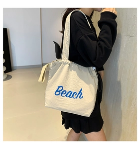 Detail of drawstring closure and blue Beach lettering on beige canvas tote bag