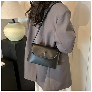 Detail of a black leather handbag featuring a silver metal bow and slim shoulder strap