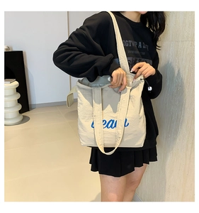 Detail of beige tote bag with blue script text, magnetic clasp and side drawstrings