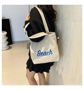 Detail of minimalist beige canvas tote bag with blue Beach lettering and wide shoulder strap