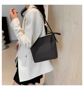 Detail of black tote bag with red heart pattern and bow, shown on shoulder over white blazer