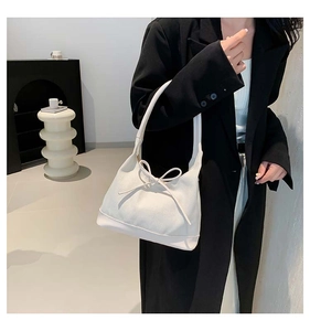 Chic cream tote bag with bow detail and leather base held by model in black blazer