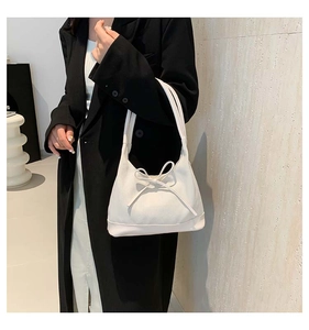 Close-up of white canvas tote bag with bow detail worn over a black blazer for a chic look