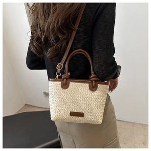 Detail einer beigen Stroh-Beuteltasche mit braunen Ledergriffen, von Model getragen