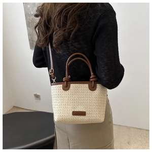 Stroh-Umhängetasche mit braunen Lederdetails am Modell in minimalistischer Umgebung