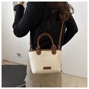 Detail of woven crossbody bag with dark brown leather handles and knot design on a model
