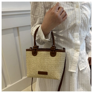 Detailed view of beige woven straw tote bag with brown leather handles and logo patch