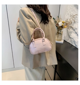 Model wearing a small light pink leather bowling bag with handle and crossbody strap