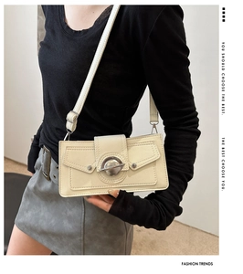 On-shoulder view of a beige rectangular crossbody bag with double flap and metal lock