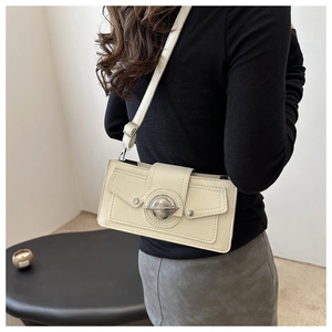 Detail view of cream rectangle leather crossbody bag with round metal lock and lychee texture