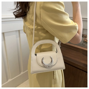 Detail of off-white crossbody bag featuring a distinctive silver crescent metal buckle closure