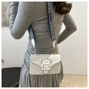 Detail der cremeweißen Umhängetasche mit breitem blauem Gurt und Fashion-Text