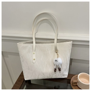 Large cream tote bag with pleated texture, gold studs and plush doll on a wood surface