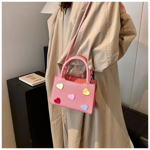 Detail of pink woven handbag with colorful heart patches and slim detachable strap