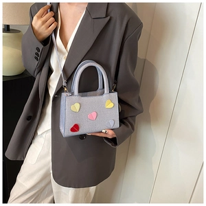 Detail of light blue woven handbag with colorful heart patches and round handle
