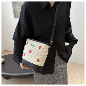 Detail of straw bucket bag featuring red strawberry embroidery and black leather straps