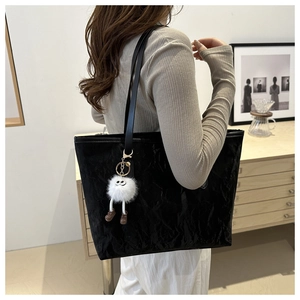 Close-up of black textured leather tote bag featuring a cute white plush monster charm