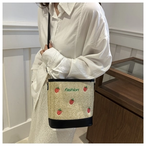 Detail of straw bucket bag with strawberry embroidery and black leather trim accents