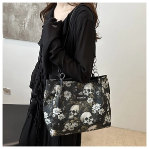 Detail of a black gothic tote bag featuring skull and floral prints with silver chain strap