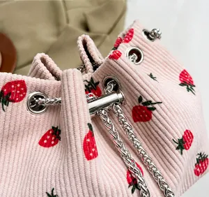 Detail of pink corduroy bucket bag featuring red strawberry embroidery and silver chain