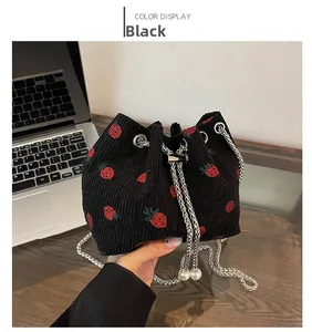 Detail of black corduroy bucket bag featuring strawberry embroidery and pearl charms