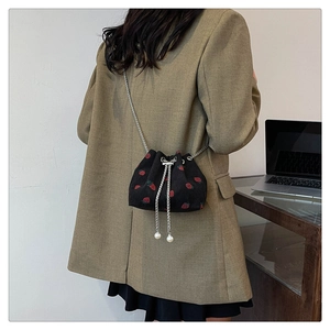 Detail view of corduroy bucket bag with strawberry print and pearl chain strap on model