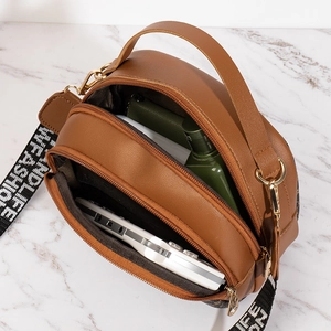 Brown round quilted crossbody bag with triple zippers and a wide printed strap