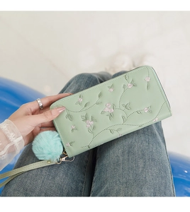 Detail der minzgrünen Damenhandtasche mit rosa Blumenstickerei und Bommel-Anhänger