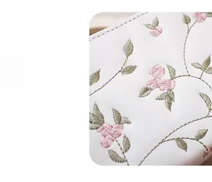 Detailaufnahme der rosa Blumenstickerei und Nähte auf einer weißen Ledergeldbörse für Damen