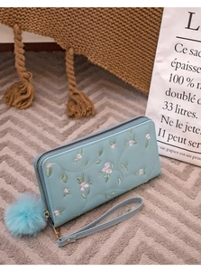 Detail einer hellblauen bestickten Geldbörse mit Blumenmuster und weichem Pelzball-Anhänger