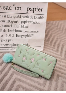 Detail der mintgrünen langen Brieftasche mit Blumenstickerei und blauem Bommel-Anhänger