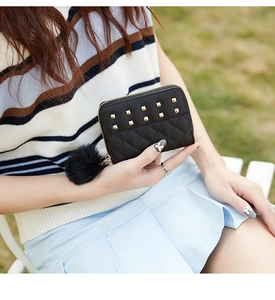 Detail of black studded quilted purse with golden zipper and plush ball charm in hand