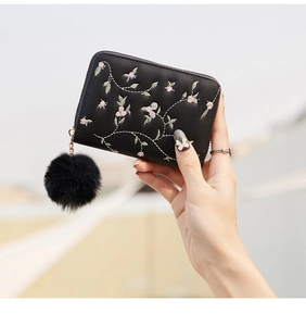 Detalle del bordado floral en cartera de cuero negro con un suave colgante de pompón