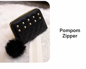 Detail of black quilted leather lady's purse featuring golden rivets and a large pompom charm