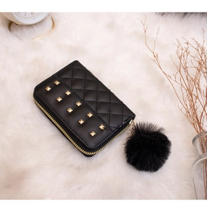 Detail of black quilted purse with gold studs and a large fluffy pompom keychain