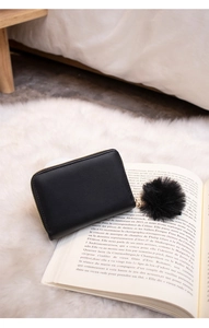 Detail of black rectangular studded wallet with a fluffy pompom keychain on an open book