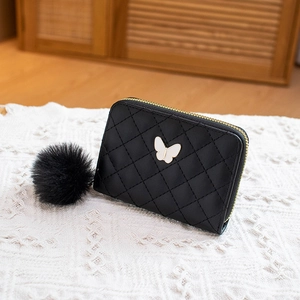 Black quilted butterfly wallet with soft pompom pendant on a rustic lace background