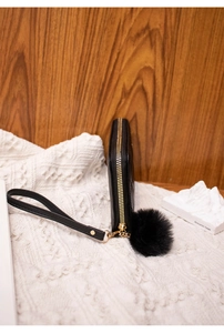 Detail view of black quilted long wallet with golden zipper, wrist strap and pompom charm
