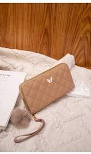 Close-up of beige quilted long wallet with butterfly decor and pompom on knit background