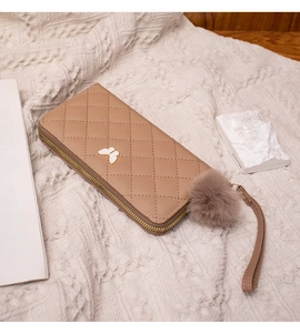 Detail of camel quilted long wallet featuring butterfly clasp and plush pom-pom charm