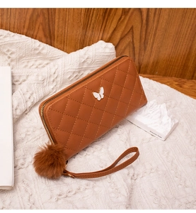 Detail of a brown quilted long wallet with a butterfly accent and soft fur ball charm