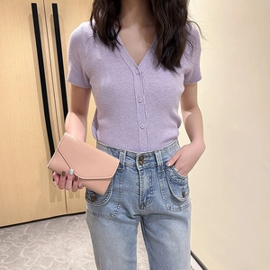 Pink envelope clutch bag paired with a lilac knit cardigan and light blue jeans