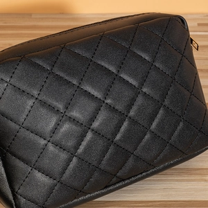 Sacoche de téléphone matelassée noire avec fermeture éclair dorée sur fond de bois